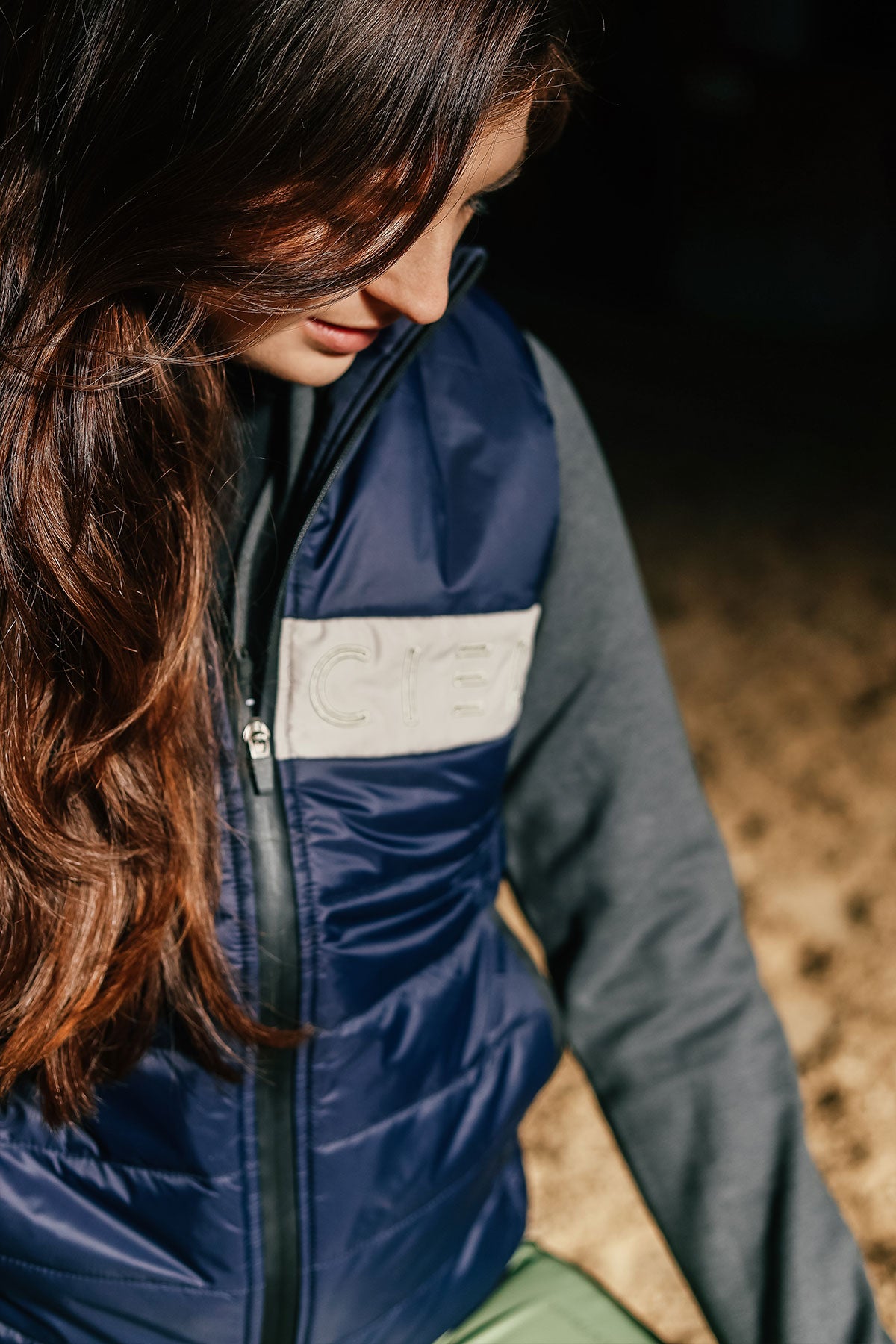 A person wearing a navy Carter Body Warmer vest with a cream Cieli logo patch on the chest, paired with a grey long-sleeved hoodie.