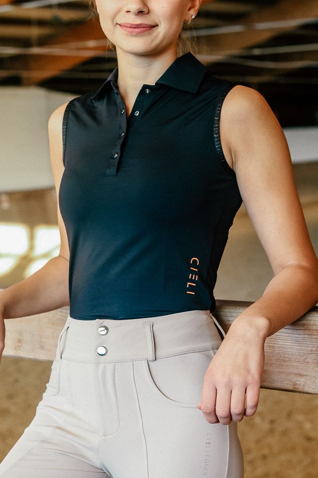 Woman wearing a black sleeveless polo shirt with a brand logo, standing indoors.