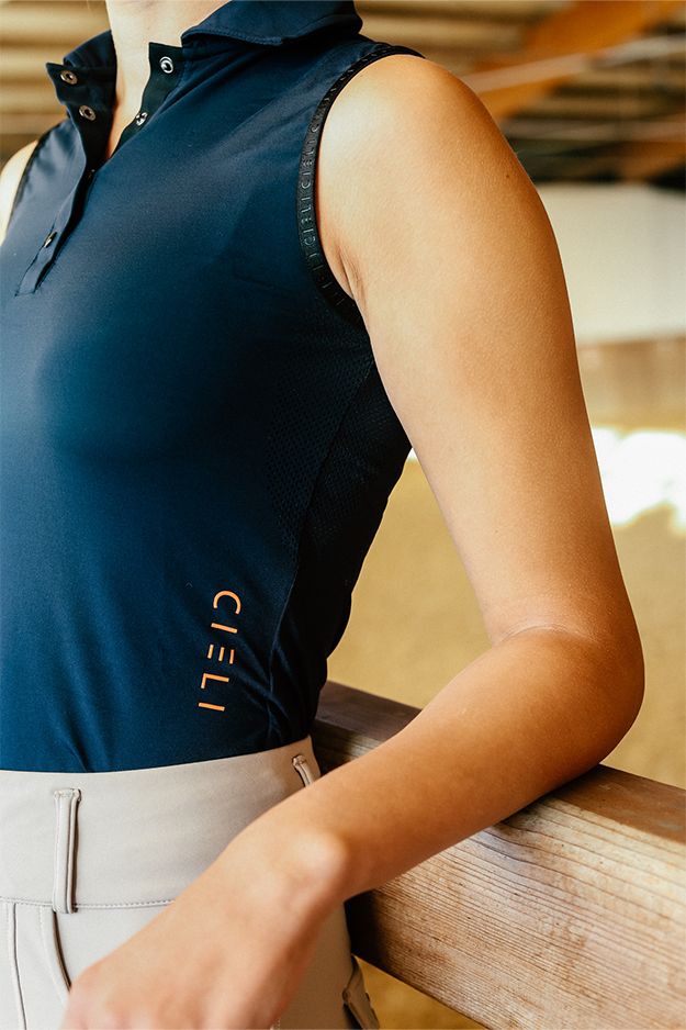 Person wearing a navy sleeveless polo shirt with 'Cieli' branding, standing against a blurred indoor background.