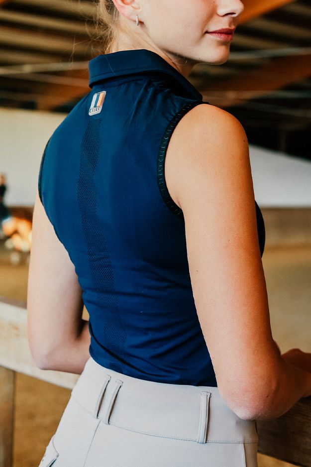 Person wearing a blue sleeveless top with a logo on the back, standing indoors.