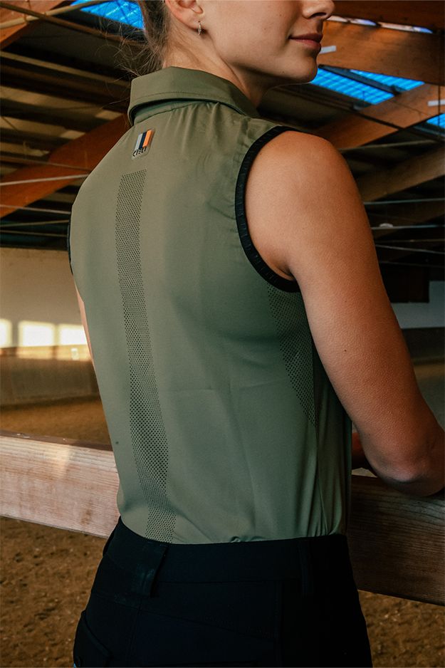 Person wearing a green sleeveless shirt with a logo on a wooden floor background
