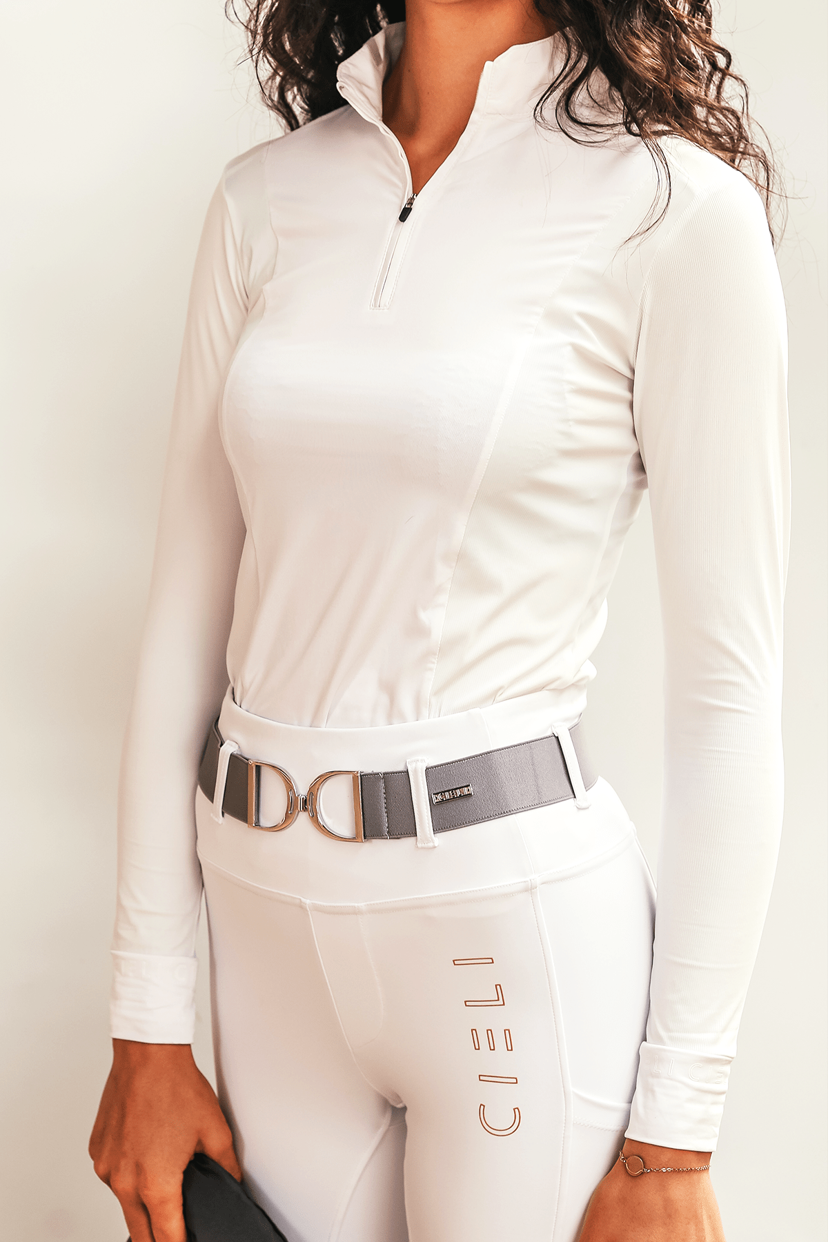 A person wearing a long sleeve show shirt in white colors, and pleats at the back. The shirt has a zipper at the neck and a belt around the waist.