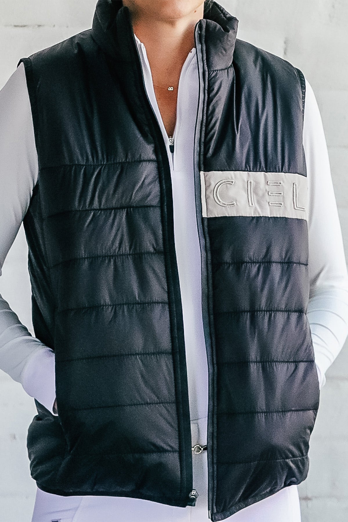 A person wearing a black and navy Carter Body Warmer vest with a cream Cieli logo patch on the chest, paired with a white long-sleeved top.