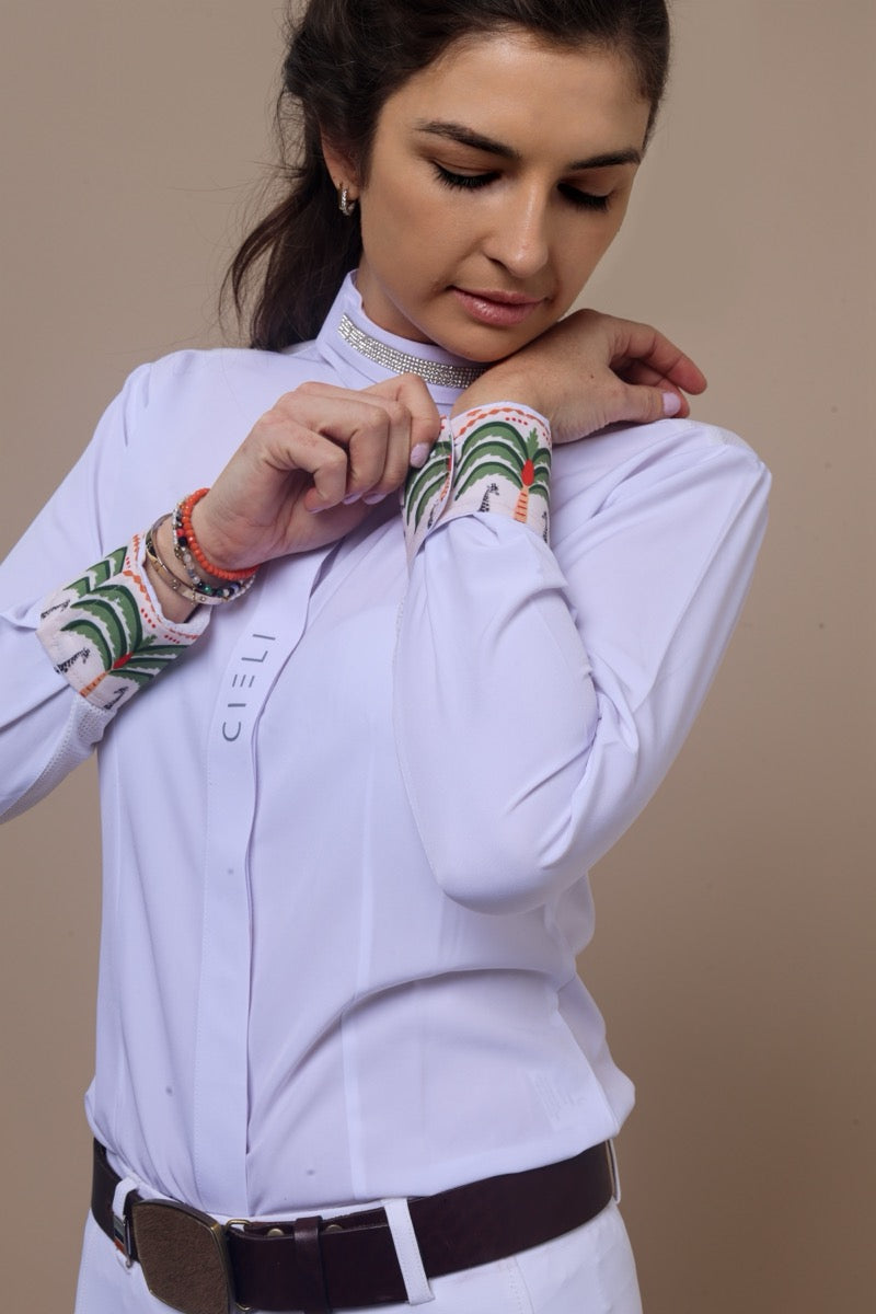 Woman wearing a white show shirt with decorative cuffs and a belt, against a beige background