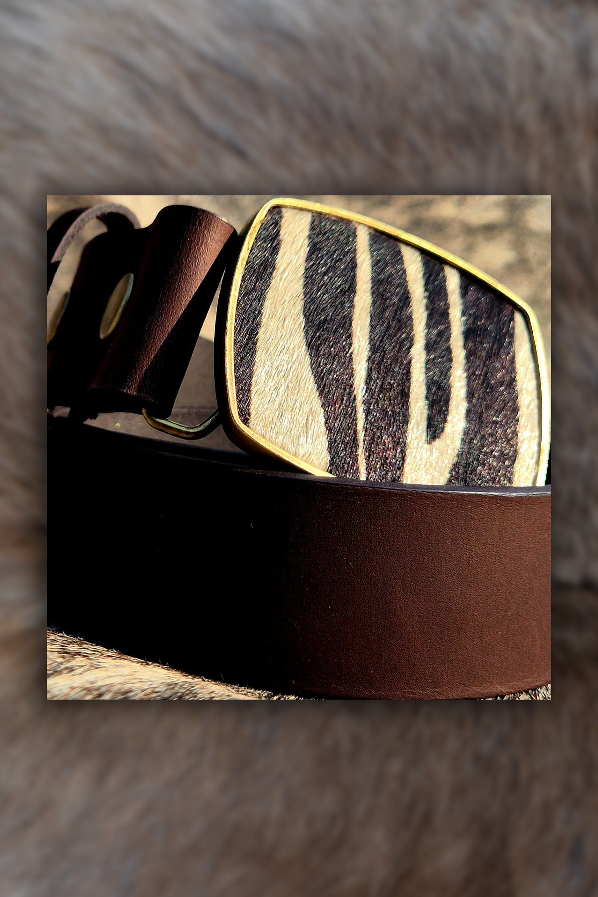 Brown leather belt with zebra pattern buckle on a fur background