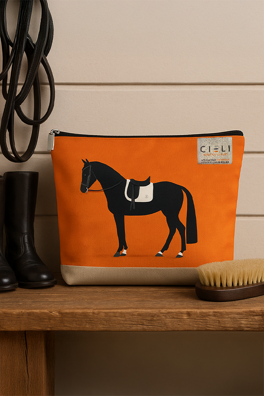 Orange pouch with horse design on a wooden surface next to black boots and a brush
