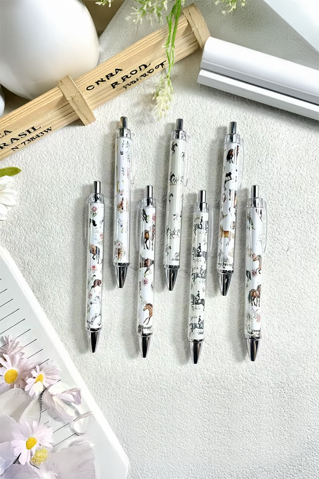 Set of pens with decorative designs on a textured surface with flowers and stationery items.