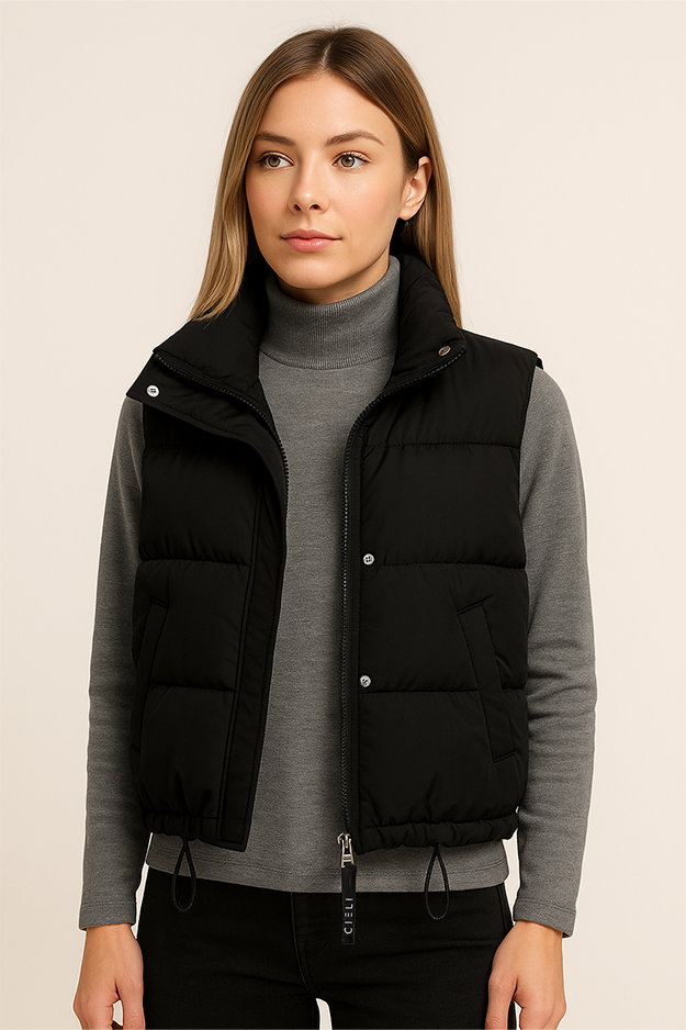 Woman wearing a black puffer vest over a gray sweater on a beige background