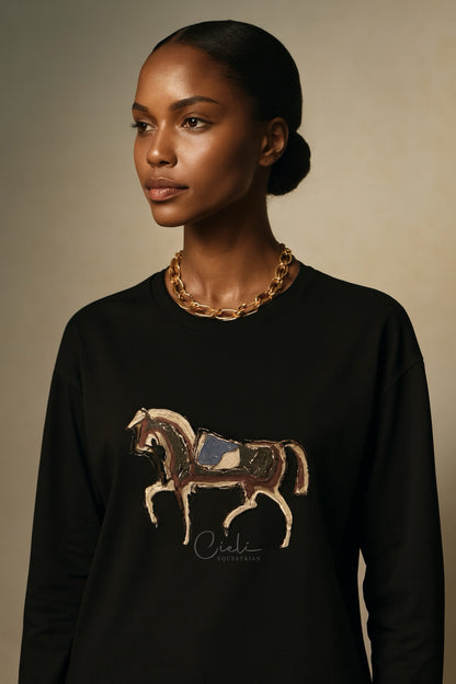 Woman wearing a black sweatshirt with a horse design and gold necklace against a beige background