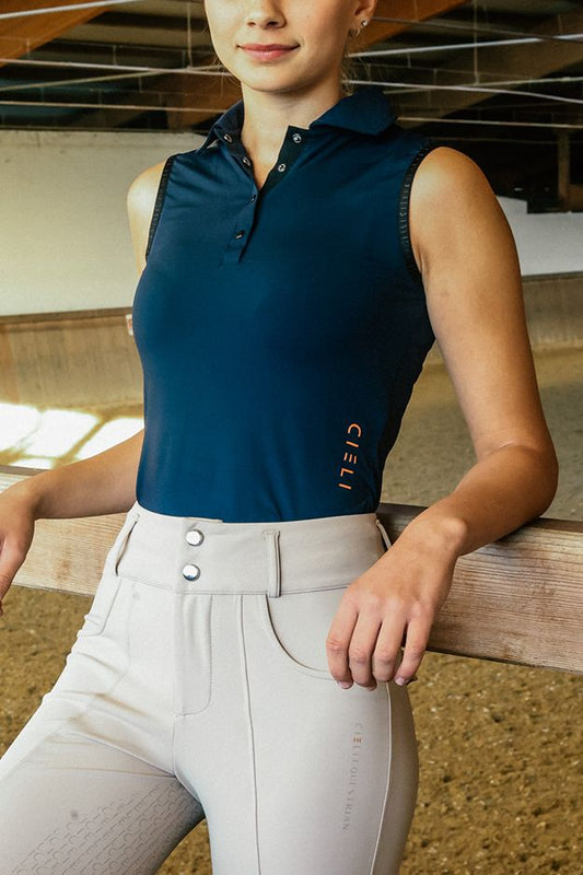 Woman in equestrian attire standing in an indoor stable.
