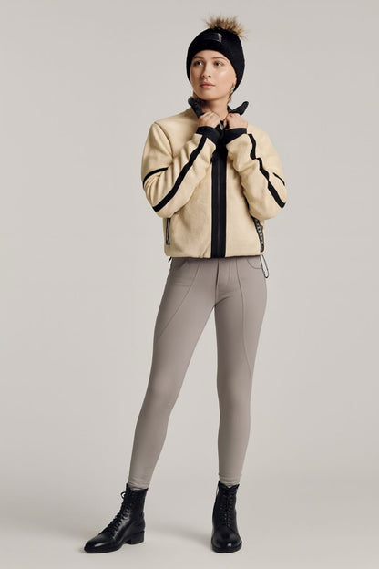 Person wearing a beige jacket with black accents, gray riding pants, and black boots on a plain background