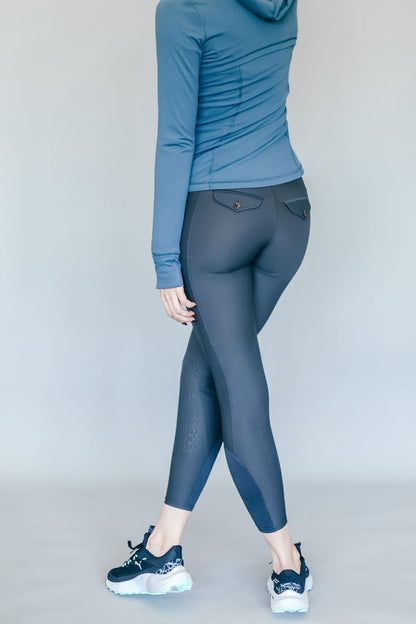 Person wearing a blue hoodie and gray breeches on a plain background
