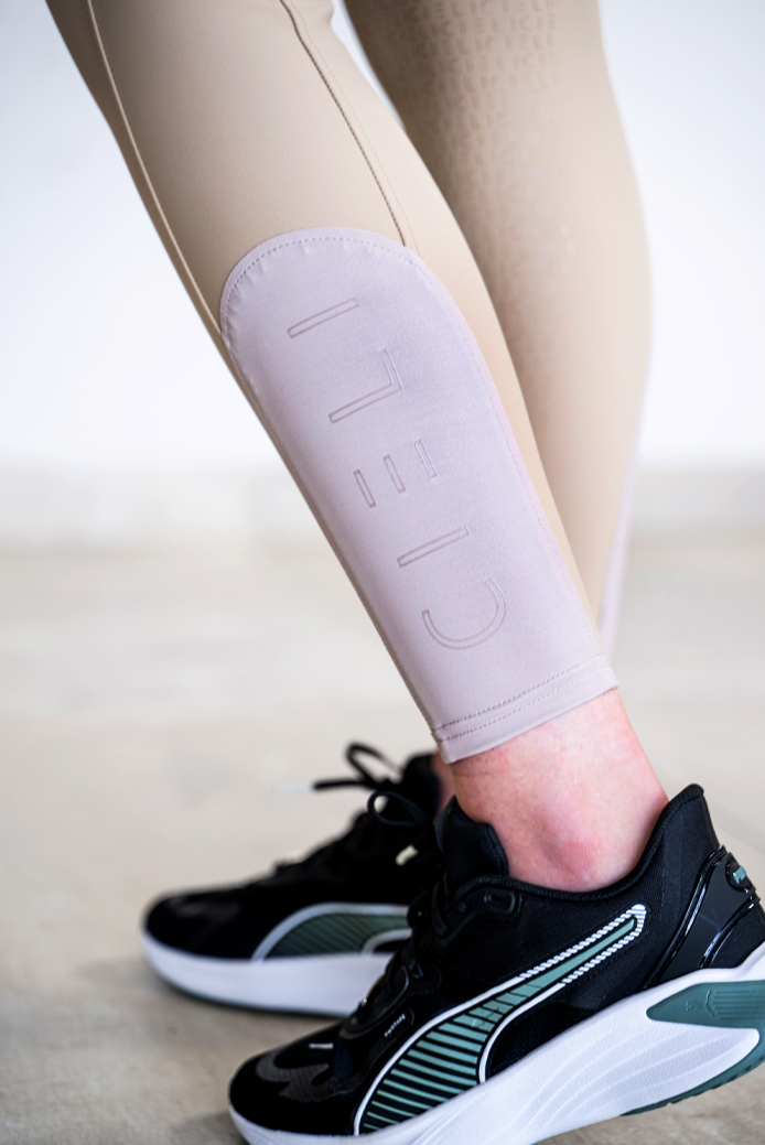 Close-up of a person's lower legs wearing beige leggings with a large tonal 'CIELI' logo on the calf, paired with black and green Puma sneakers.