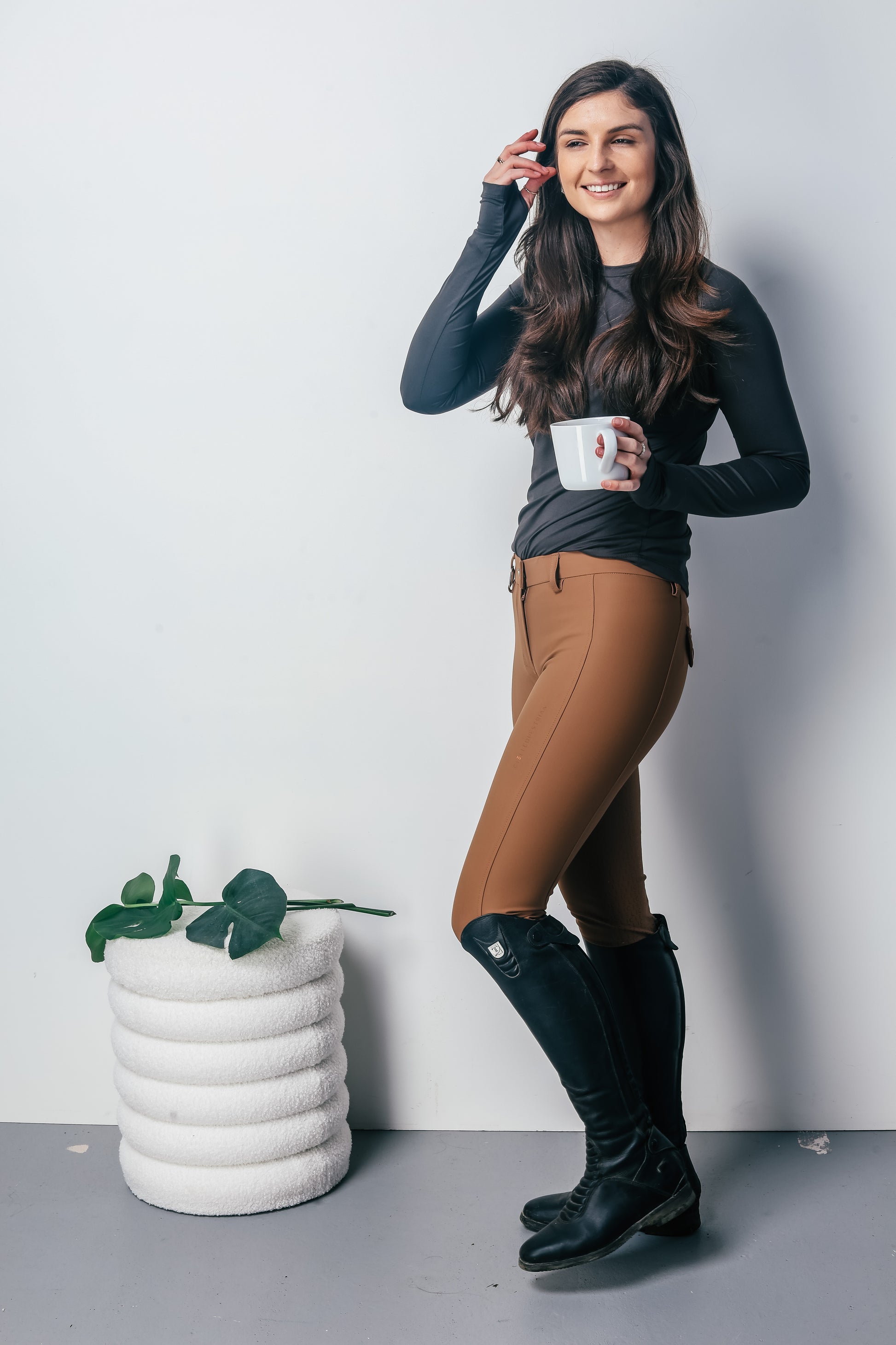Woman in equestrian attire holding a mug against a plain background