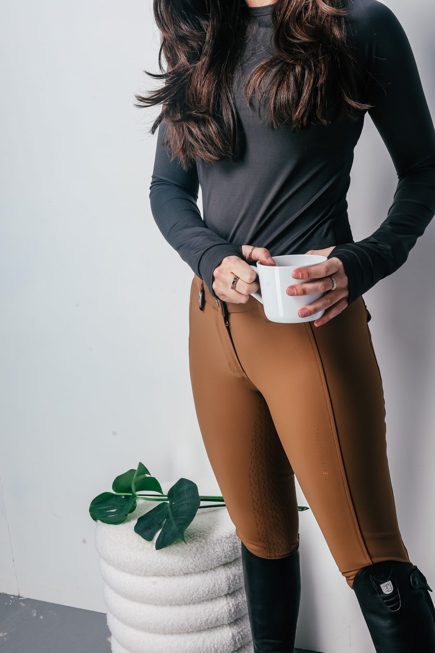 Person wearing a grey long-sleeve top and brown breeches holding a white mug.