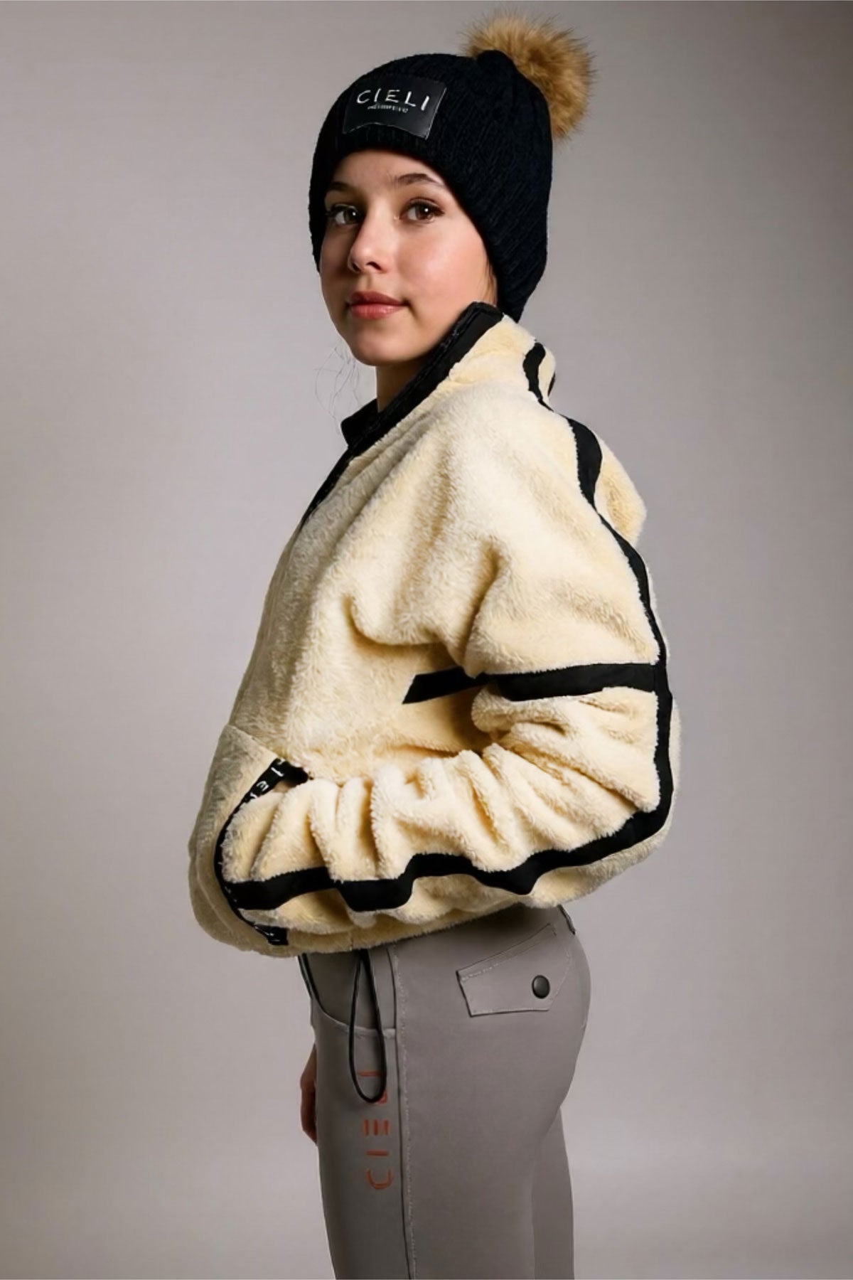 Person wearing a cream-colored fleece jacket with black accents, standing against a plain background.