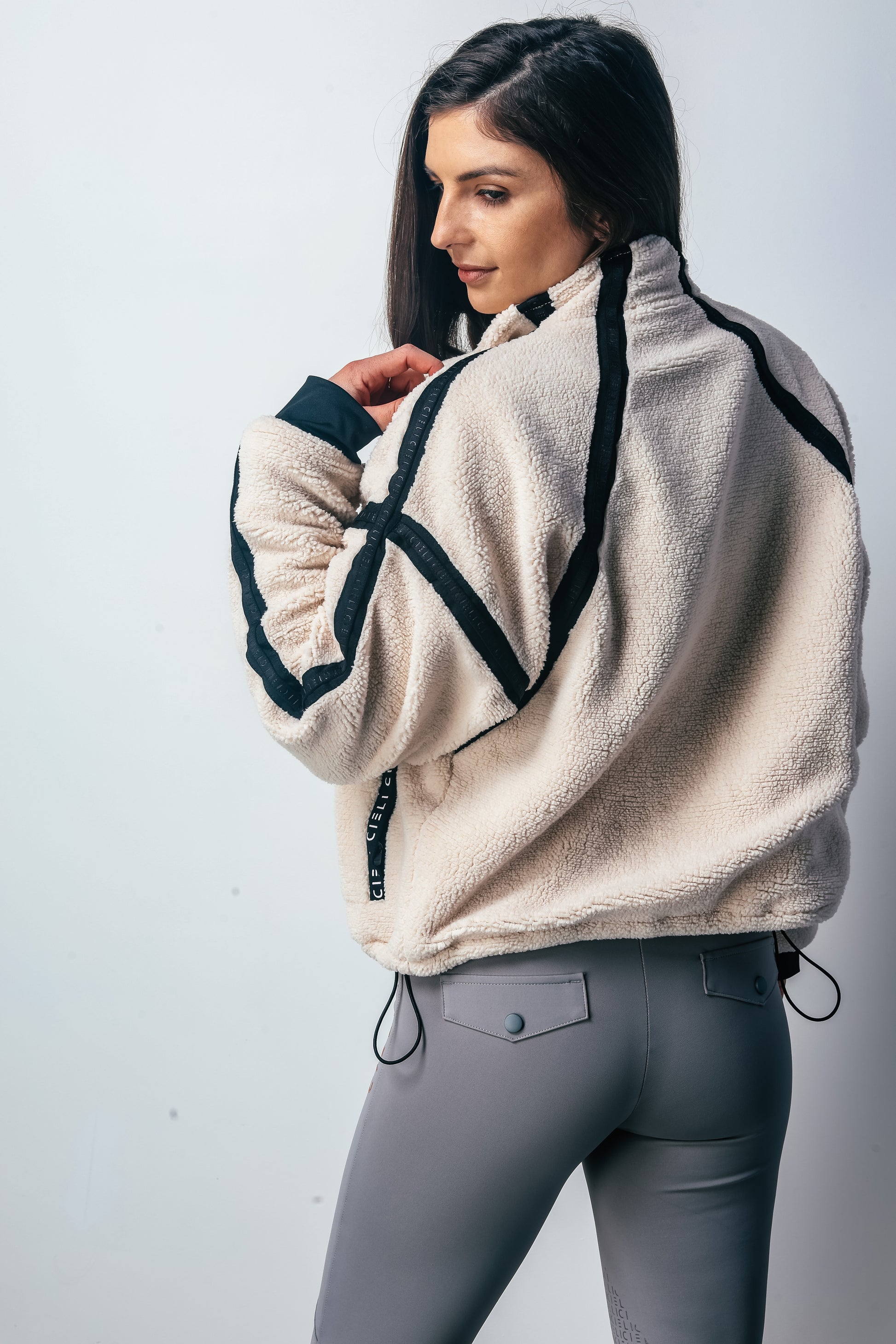 Woman wearing a beige fleece jacket with black accents on a white background