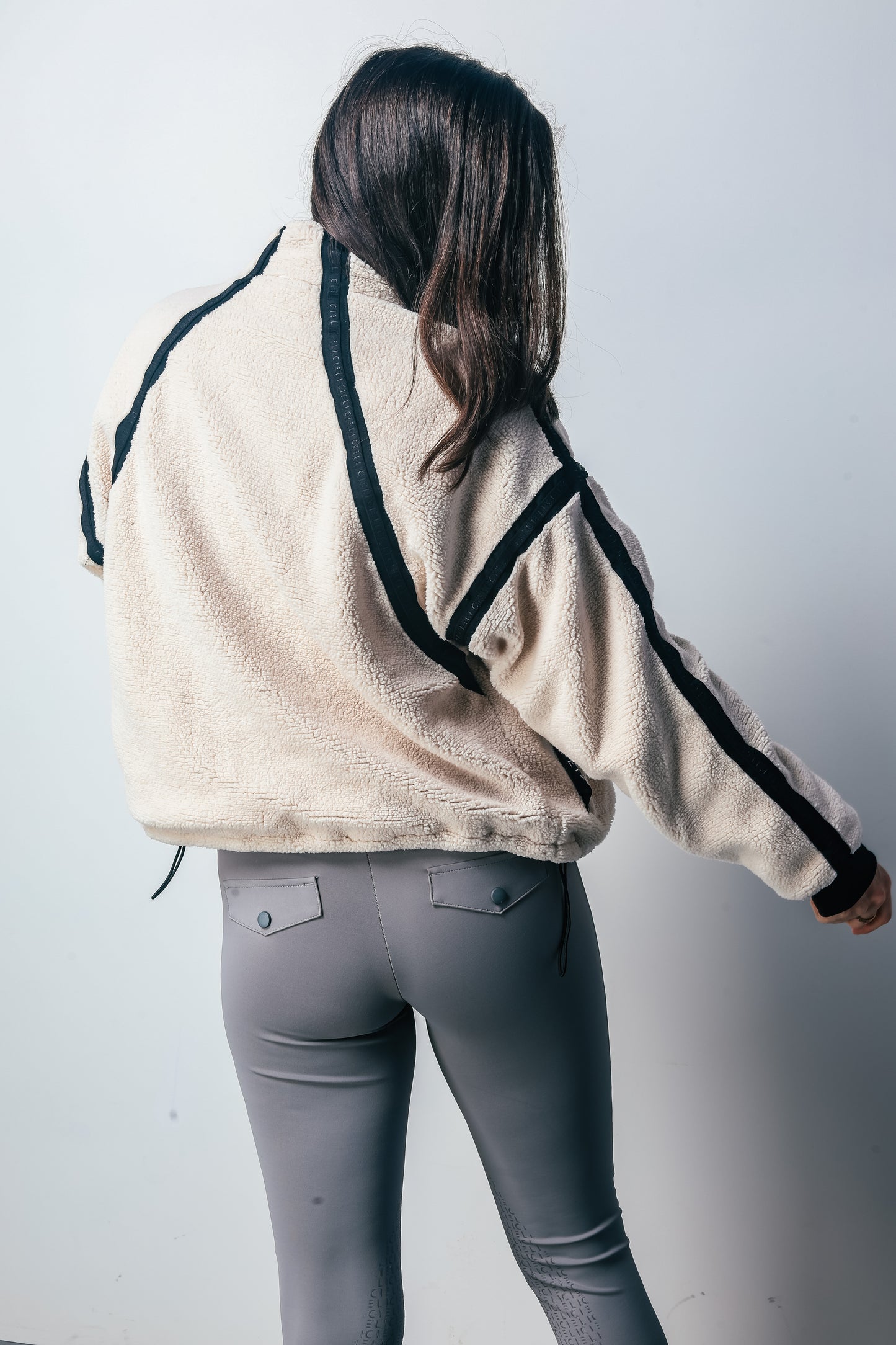 Person wearing a beige jacket with black accents and gray pants on a white background
