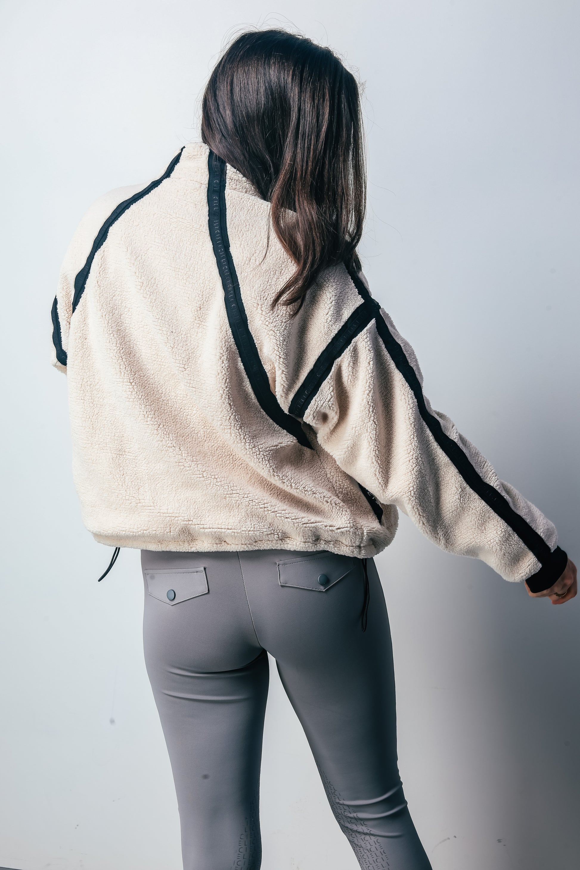 Person wearing a beige jacket with black accents and gray pants on a white background