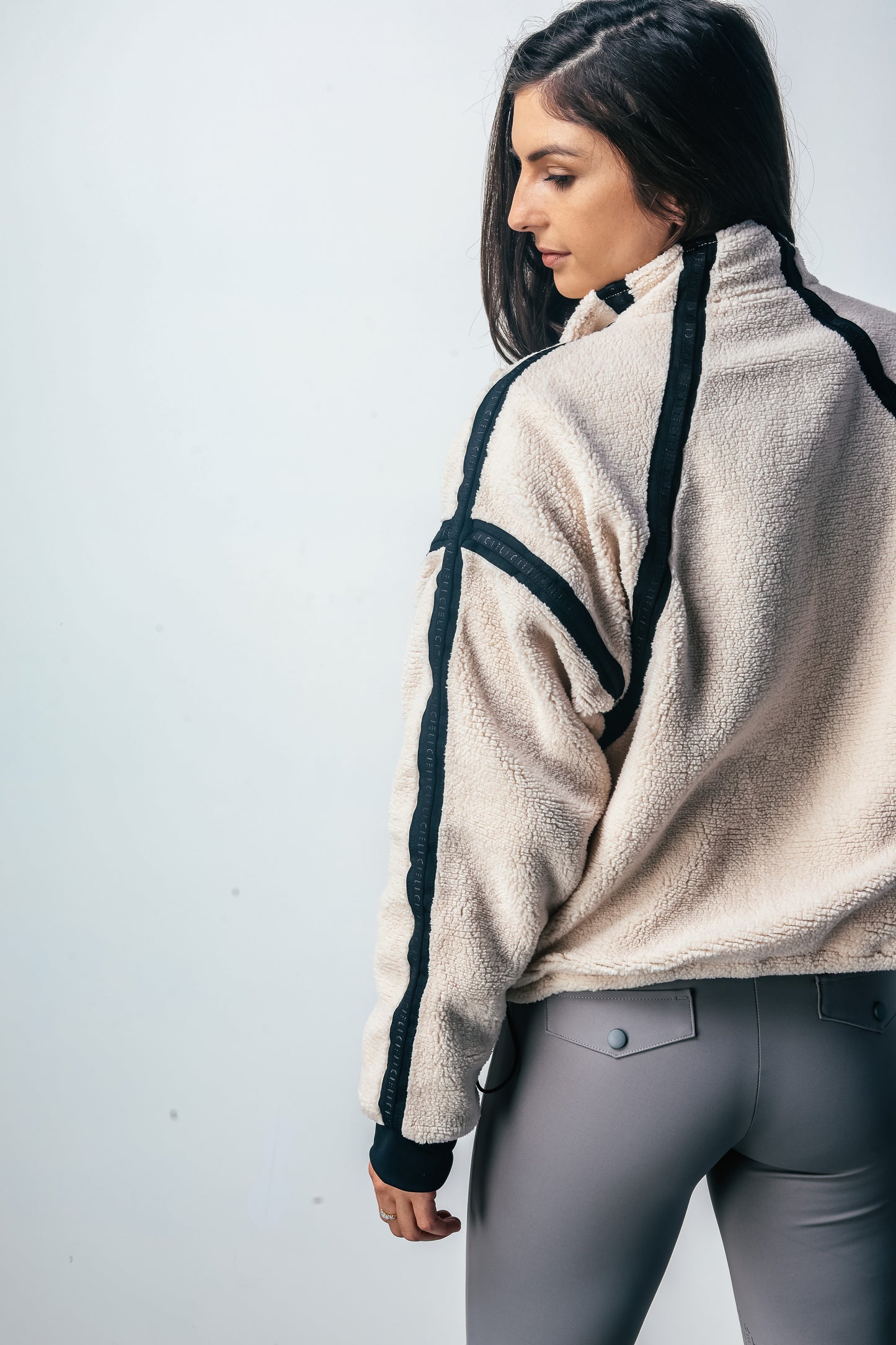 Woman wearing a beige fleece jacket with black accents on a white background