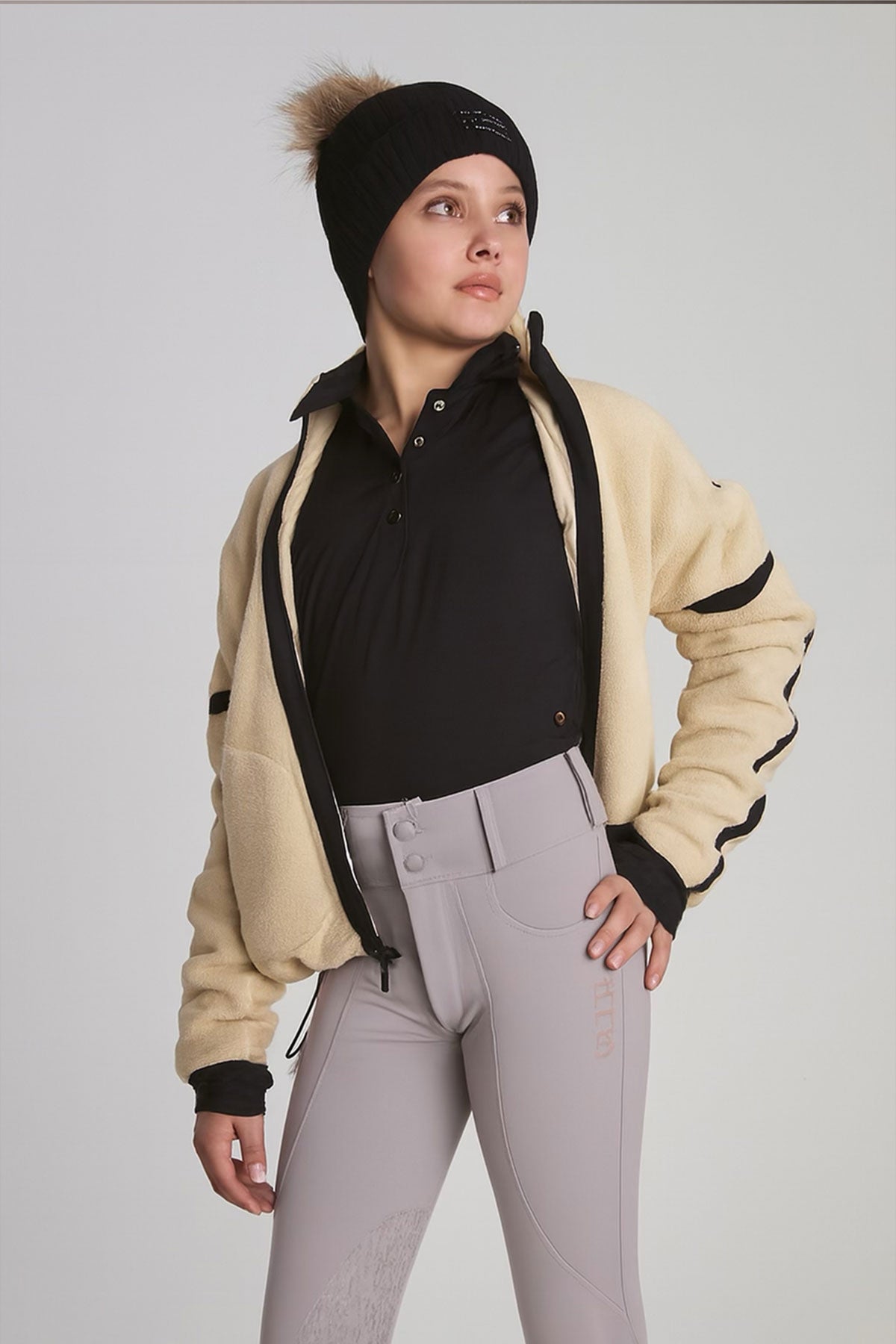 Person wearing a beige fleece jacket, black shirt, and gray pants on a plain background