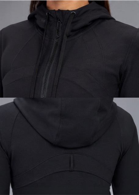 A close-up of a black athletic zip-up hoodie shown from the front and back, featuring a high collar, hood, and zippered front, on a model against a neutral gray background.