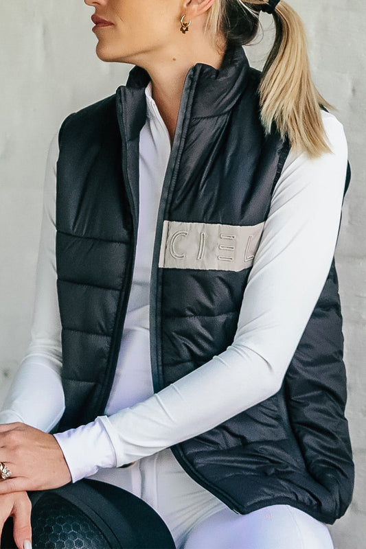A person wearing a black and navy Carter Body Warmer vest with a cream Cieli logo patch on the chest, paired with a white long-sleeved top.