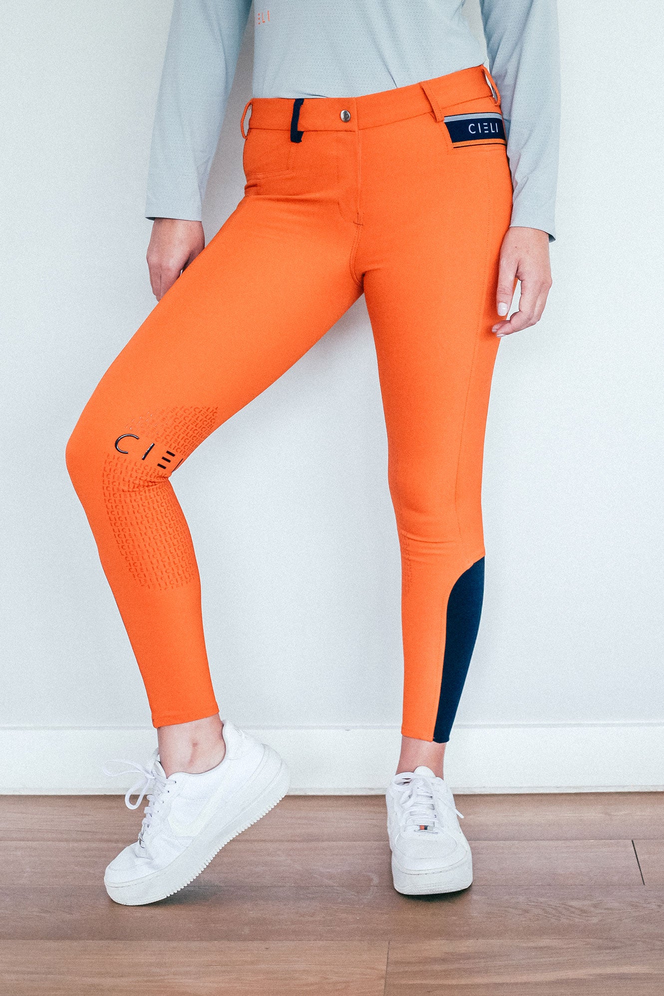 Lady wearing everyday orange equestrian pants, resembling a sporty twist on modern riding breeches.