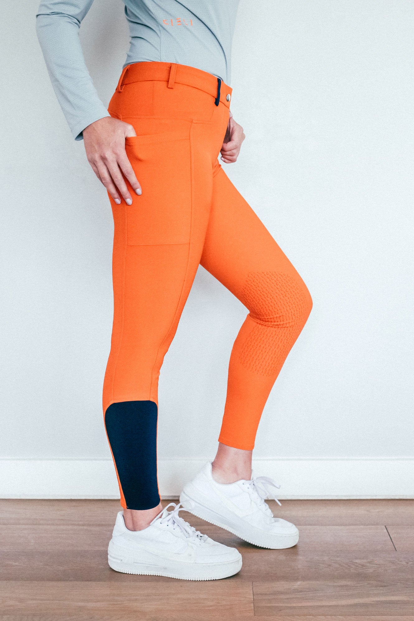 Lady wearing everyday orange equestrian pants, resembling a sporty twist on modern riding breeches.