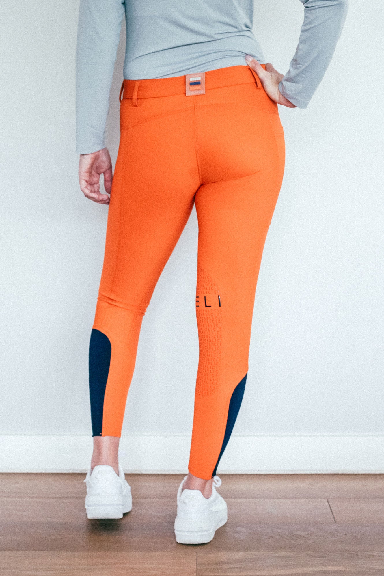 Lady wearing everyday orange equestrian pants, resembling a sporty twist on modern riding breeches.