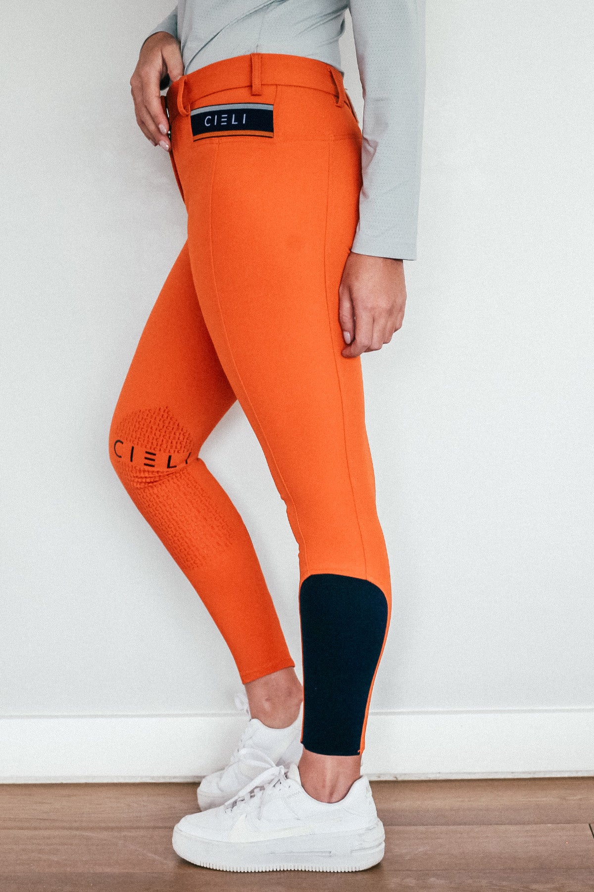 Lady wearing everyday orange equestrian pants, resembling a sporty twist on modern riding breeches.